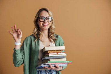 Çekici, mutlu, gözlüklü, gri arka planda izole edilmiş ders kitaplarını tutan genç bir kadın portresi. Eğitim fakültesi konsepti. Pozitif duygular, yüz ifadesi