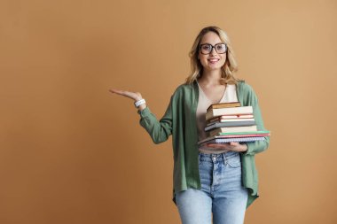 Çekici, mutlu, gözlüklü, gri arka planda izole edilmiş ders kitaplarını tutan genç bir kadın portresi. Eğitim fakültesi konsepti. Kopyalama alanı sunuluyor