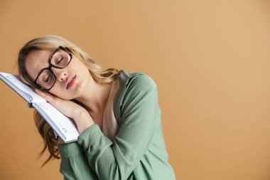 Gözlüklü, bej duvarda izole edilmiş takvimle uyuyan yorgun ve güzel bir kadın.