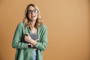 Gözlüklü mutlu bir kadın, bej duvarda izole edilmiş bir takvimle poz verirken gülüyor.