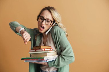 Bej duvarda izole bir şekilde cep telefonuyla konuşurken kol saatine bakan sürpriz bir kadın.