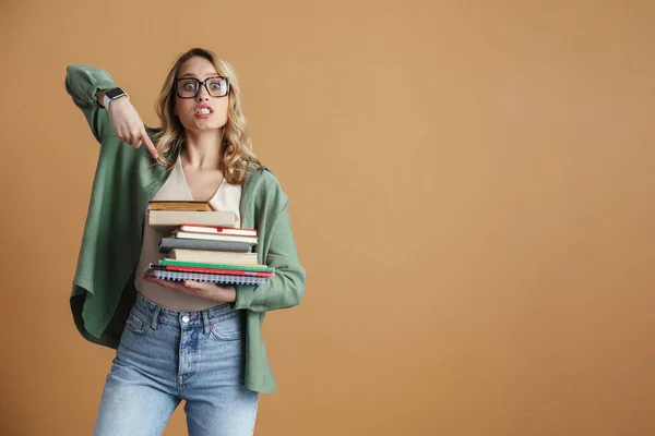 严肃的年轻女子戴着眼镜 用手指着手中的一堆书 这些书被灰色的背景隔开了 — 图库照片