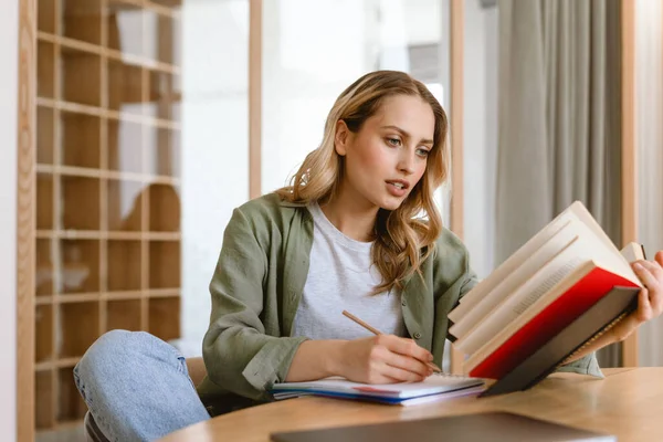 Düşünceli Genç Sarışın Bir Kadın Elinde Kitapla Tahta Masada Otururken — Stok fotoğraf