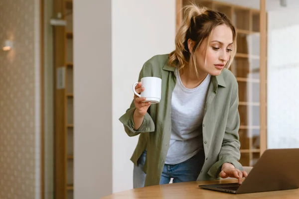 若い白人女性はコーヒーを飲み 自宅でラップトップを使用して — ストック写真