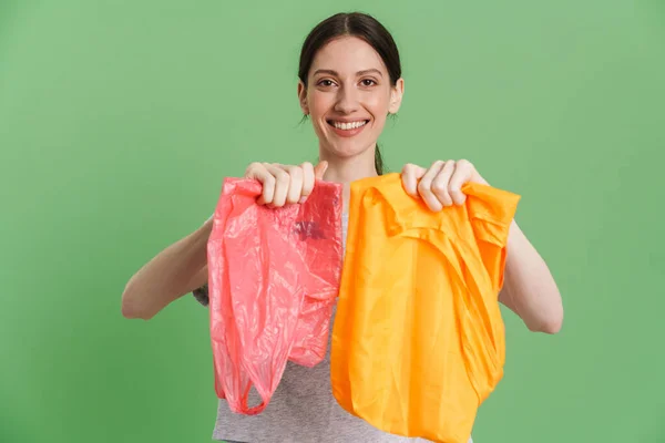 Mladá Bruneta Žena Ukazuje Plastové Textilní Tašky Izolované Přes Zelené — Stock fotografie