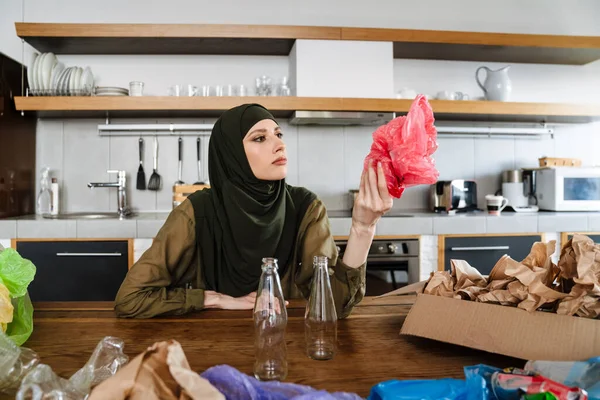 年轻的穆斯林妇女坐在厨房的桌子旁 头戴头巾 对废物进行分离 — 图库照片