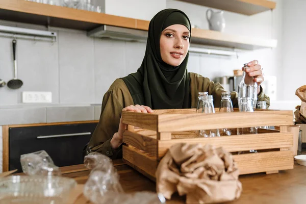 穿着头巾 对玻璃瓶和塑料容器进行分类 在厨房里循环利用 微笑着的伊斯兰妇女 — 图库照片