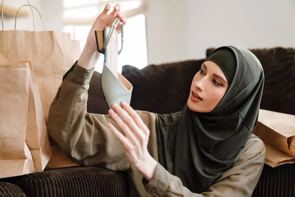 年轻的穆斯林妇女坐在家里的地板上 头戴头巾 拿着鞋子 — 图库照片