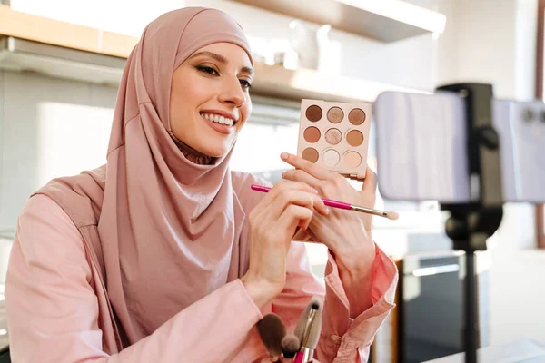 穿着头巾的年轻穆斯林女性在家里用手机相机为她的化妆品博客制作了一个视频 对化妆品大肆宣扬一番 — 图库照片