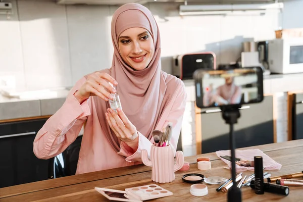 穆斯林妇女在家里展示美容产品的同时 还在手机上自拍了一段视频 — 图库照片