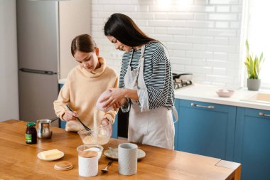 Mutfakta krep hamuru yaparken gülümseyen güzel anne ve kız.