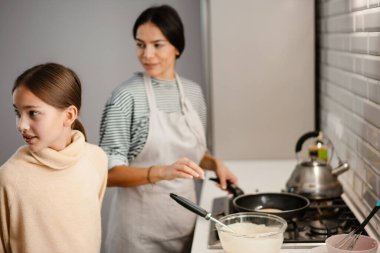 Güzel bir anne ve kız, sıcak mutfakta krep pişiriyor.