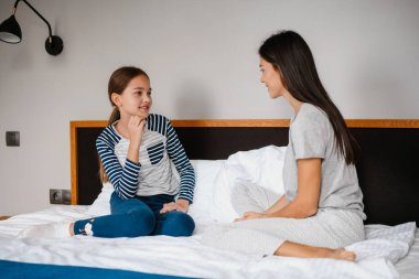 Mutlu güzel anne ve kız evdeki yatakta otururken konuşuyor.
