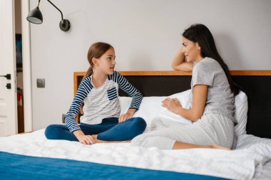 Mutlu güzel anne ve kız evdeki yatakta otururken konuşuyor.
