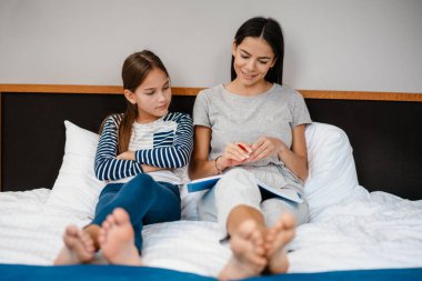 Güzel bir anne ve kız evde yatakta otururken ödev yapıyor.