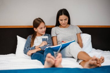 Güzel bir anne ve kız evde yatakta otururken ödev yapıyor.