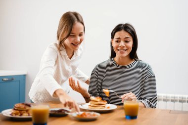 Neşeli, güzel bir anne ve kız kahvaltı yaparken eğleniyorlar.