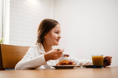 Cep telefonundan film izlerken kahvaltı yapan küçük kız.
