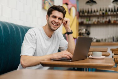 Kafede dizüstü bilgisayarla oturan gülümseyen genç bir öğrenci.