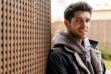 Dışarıdaki bir duvara yaslanırken kameraya bakan sıradan bir delikanlının fotoğrafını çek.