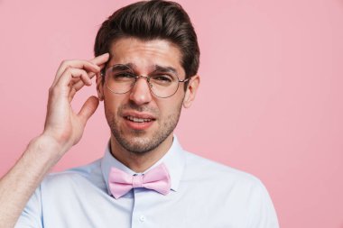 Gözlüklü, başı ağrıyan, tapınağını ovalayan, pembe arka planda yaşayan genç beyaz bir adam.