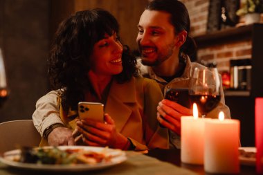 Beyaz çift evde romantik bir buluşma sırasında cep telefonu kullanıyor.