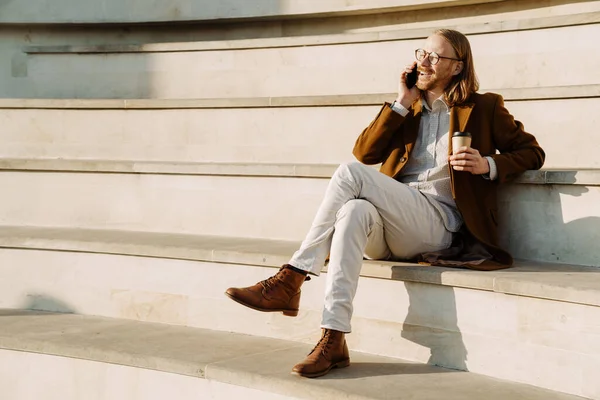Rudzielec Rozmawia Przez Telefon Komórkowy Pije Kawę Siedząc Schodach Zewnątrz — Zdjęcie stockowe