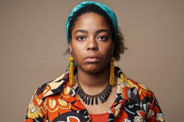 Saçbantlı genç siyah kadın gri arka planda yalnız poz veriyor ve kameraya bakıyor.