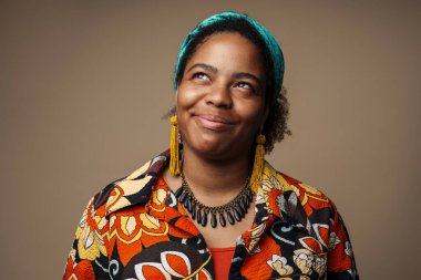 Saçbandı takmış, gülümseyen ve yukarı bakan genç siyahi kadın gri arka planda soyutlanmış.