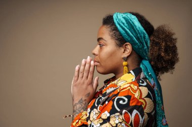 Avuç içlerini bir arada tutan genç siyahi kadın, gri arka planda tek başına poz veriyor.