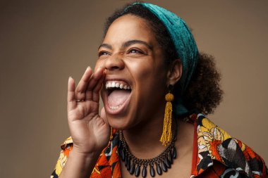 Saçbandı takmış genç siyahi bir kadın gri arka planda izole bir şekilde el kol hareketi yapıyor ve çığlık atıyor.