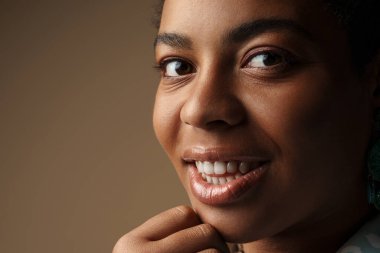 Gri arka planda izole edilmiş, gülümseyen ve kameraya bakan genç siyahi kadın.