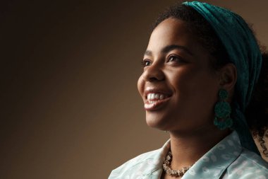 Saçbandı takmış, gülümseyen ve gri arka planda soyutlanmış genç siyah bir kadın.