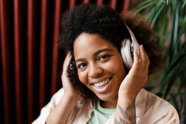Evde kulaklıkla müzik dinlerken gülümseyen genç siyahi kadın.