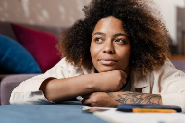 Genç siyahi kadın evde yatarken yan bakıyor.