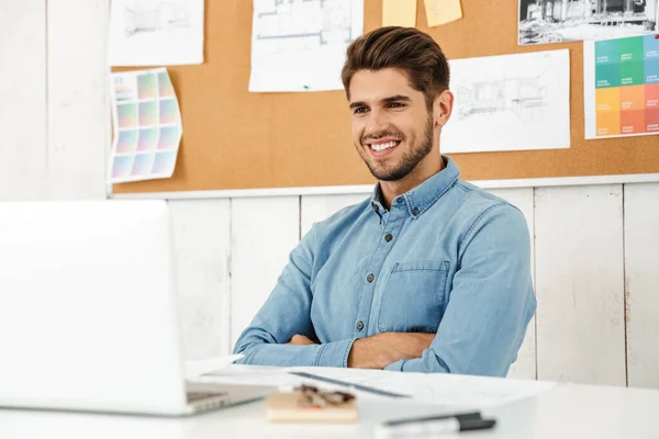 Junger Weißer Mann Lächelt Während Büro Mit Laptop Und Zeichnungen — Stockfoto