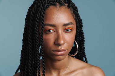 Makyajlı gömleksiz siyah kadın mavi arka planda izole edilmiş kameraya bakıyor.