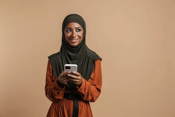 Młoda Muzułmanka Hidżabie Uśmiechnięta Podczas Korzystania Telefonu Komórkowego Odizolowana Beżowym — Zdjęcie stockowe