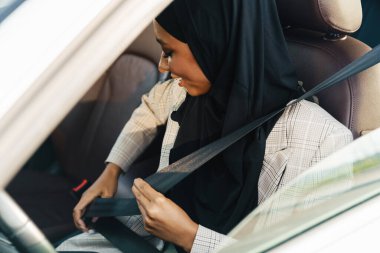 Siyah Müslüman kadın arabada otururken türban takıyor emniyet kemerini takıyor.