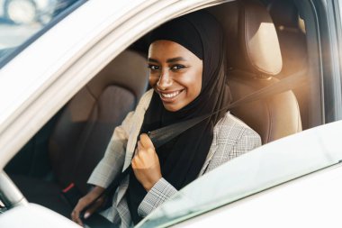 Siyah Müslüman kadın arabada otururken türban takıyor emniyet kemerini takıyor.