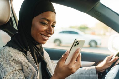 Siyah Müslüman kadın araba kullanırken başörtüsü takıyor.