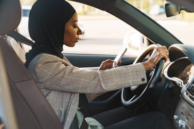 Siyah Müslüman kadın araba kullanırken başörtüsü takıyor.