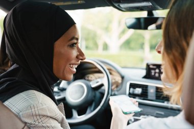İki çok ırklı kadın arabada otururken konuşup gülüyor.