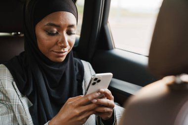 Arabadayken cep telefonu kullanan başörtüsü takan siyah Müslüman kadın.