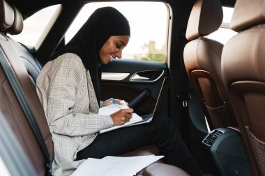 Siyah Müslüman kadın başörtüsü takıyor. Arabadayken notlar yazıyor.