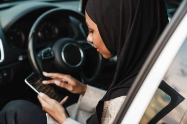 Siyah Müslüman kadın arabada otururken cep telefonu kullanıyor.