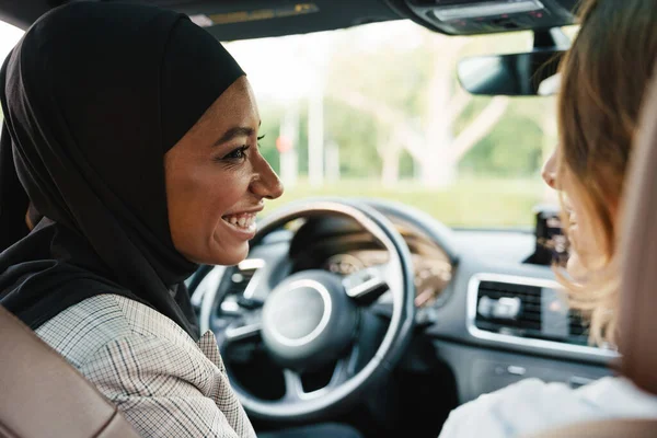 İki çok ırklı kadın arabada otururken konuşup gülüyor.