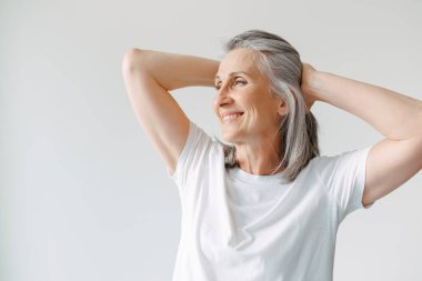 Gri tişörtlü, gülümseyen ve beyaz arka planda tek başına duran son sınıf öğrencisi kadın.