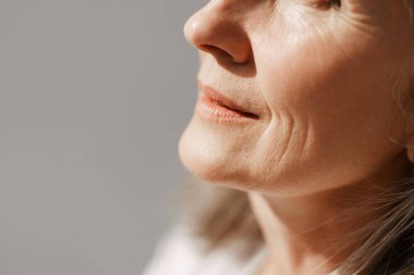 Gri yaşlı kadın beyaz arka planda poz veriyor ve bir kenara bakıyor.