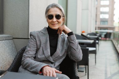 Gri beyaz yaşlı kadın gülümsüyor ve kafede otururken